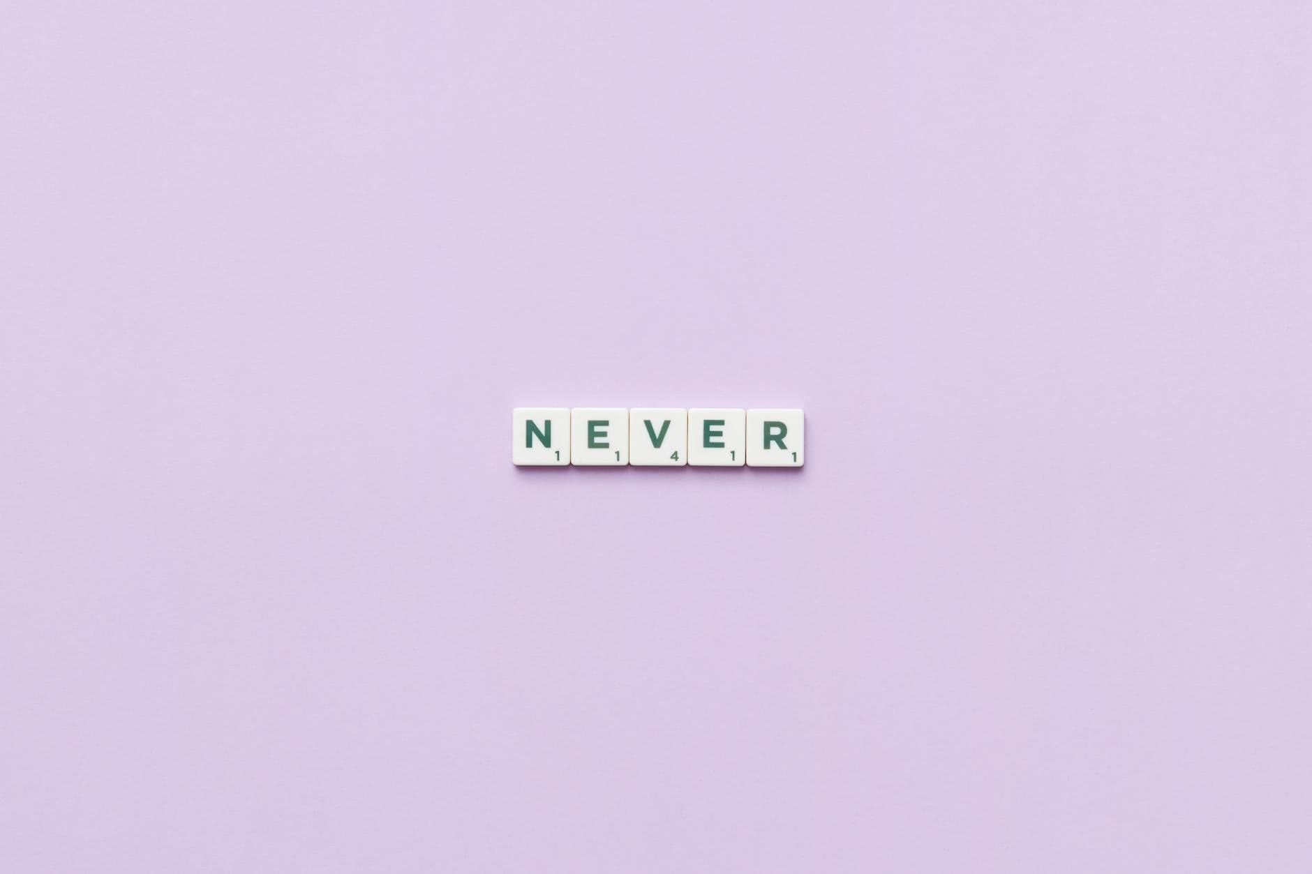 Scrabble tiles spelling 'Never' on a pastel purple background, offering plenty of copyspace.